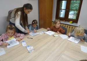 Czworo dzieci maluje na płótnie. Pani Ania jest pochylona nad stołem.